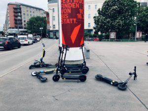 Mehrere E-Scooter liegen am Gehsteig herum oder lehnen an einer Litfaßsäule