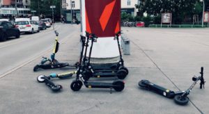 Mehrere E-Scooter liegen am Gehsteig herum oder lehnen an einer Litfaßsäule