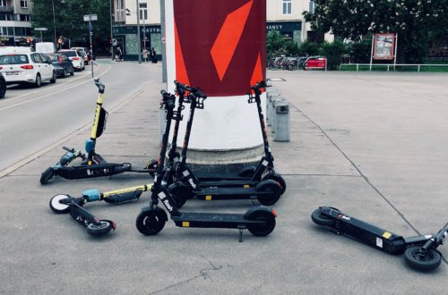 Mehrere E-Scooter liegen am Gehsteig herum oder lehnen an einer Litfaßsäule