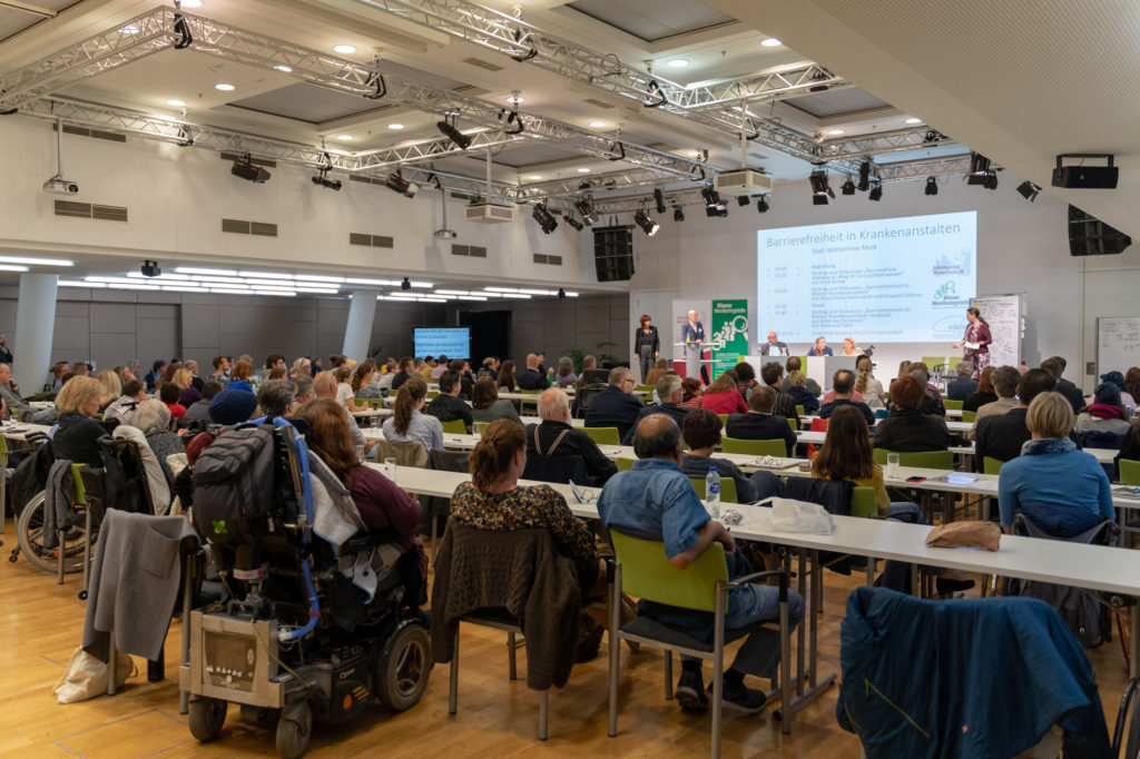 Der volle Veranstaltungssaal. Man sieht das Publikum von hinten.