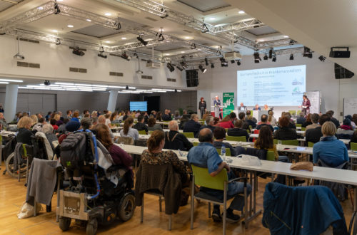 Der volle Veranstaltungssaal. Man sieht das Publikum von hinten.